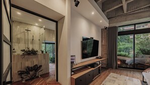 Ein modernes Wohnzimmer mit großem Fernseher, Holzböden und Blick ins Grüne.