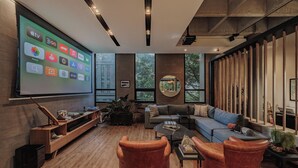 Ein modernes Wohnzimmer mit einem großen Bildschirm, der verschiedene App-Symbole zeigt, einem gemütlichen Sofa, Ledersesseln und einem Holzregal.