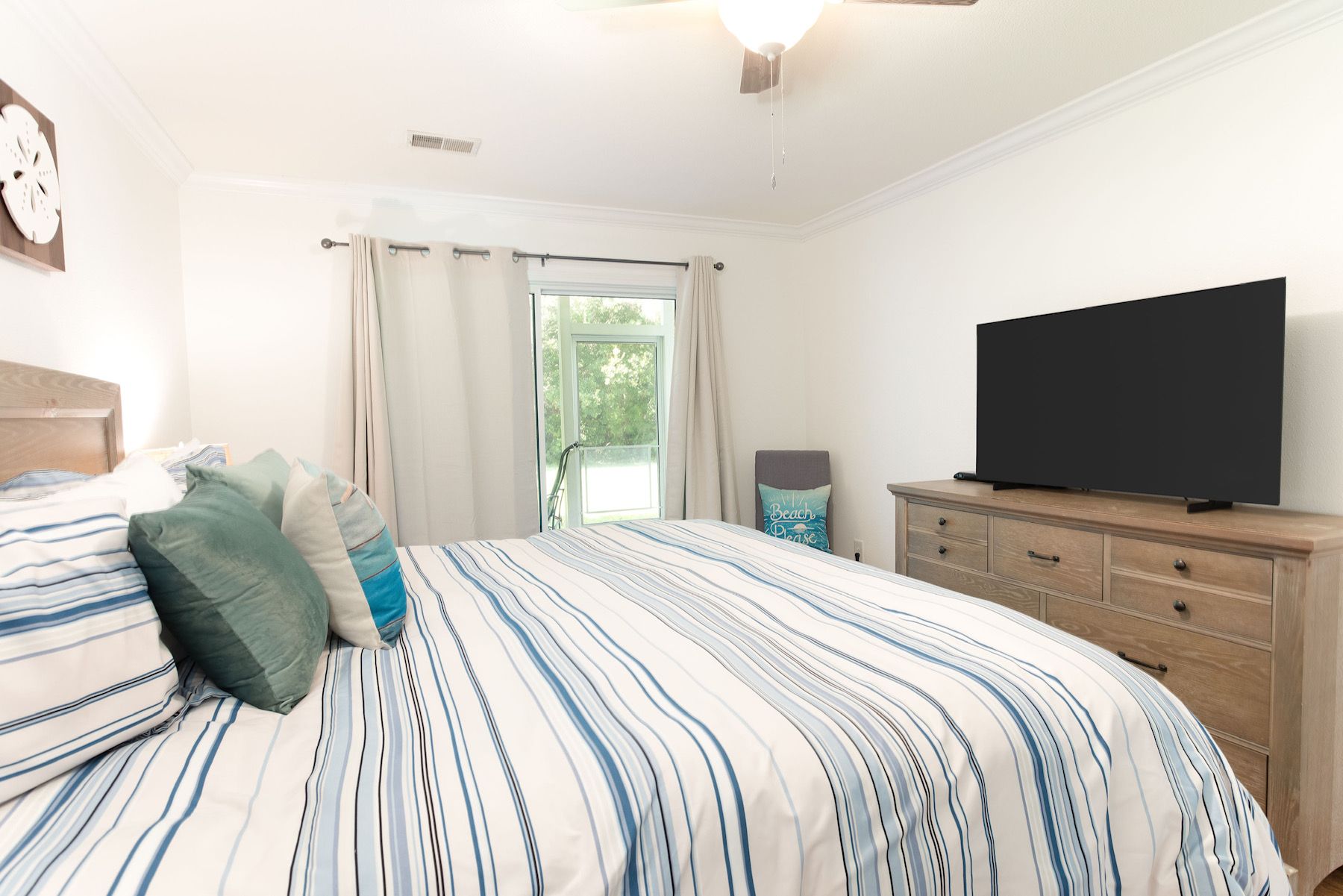 Une chambre à coucher avec un lit, un téléviseur posé sur une commode en bois et une fenêtre avec des rideaux.