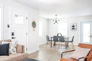 A modern living room with a beige sofa, a dining table with four chairs, and a coffee table.