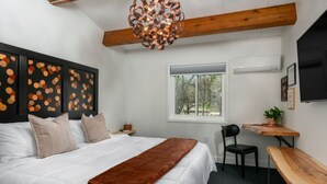 A modern bedroom with a large bed, a wooden desk, and a view of trees through a window.