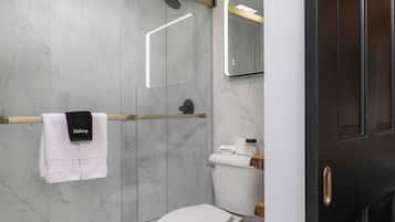 Een moderne badkamer met een marmeren wand, een wit toilet, een handdoekrek met een handdoek met de tekst 'Makeup', een spiegel en een douchehoek.