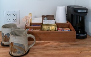 A wooden tray with coffee cups, a coffee maker, and various coffee pods on a wooden table.