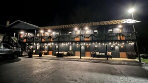 A two-story building with balconies, string lights, and a car parked in front.