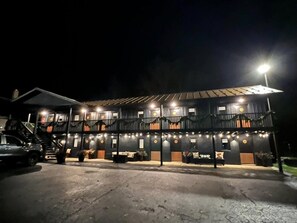 A two-story building with balconies, string lights, and a car parked in front.