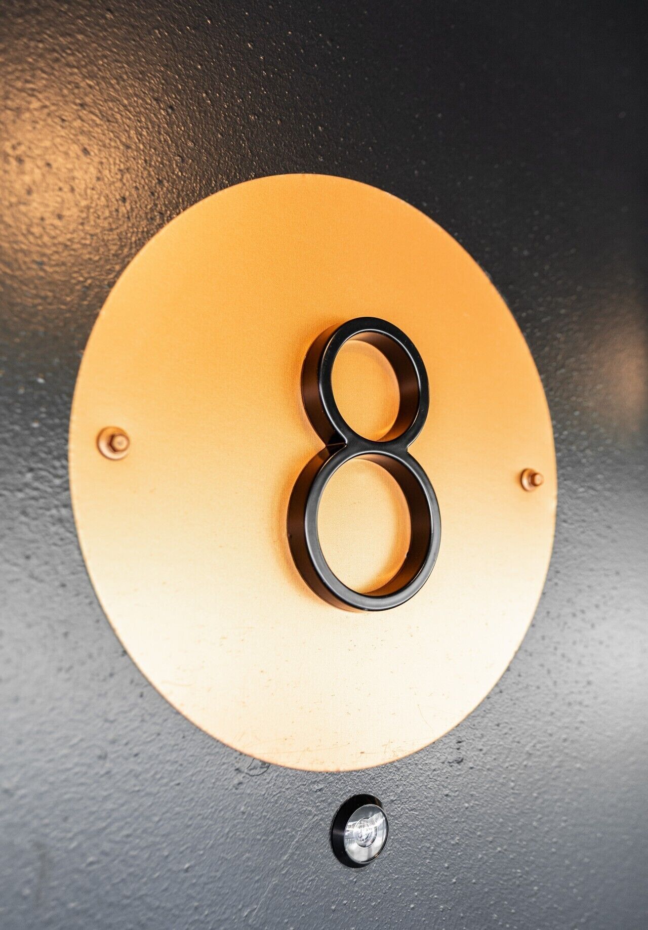 Una pared negra con una placa circular dorada que muestra el número '8' en una tipografía negra y metálica.