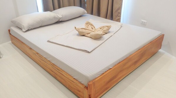 Un lit bien fait, avec un cadre en bois, un matelas blanc et une couverture pliée.