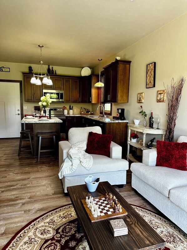A living room with a chessboard, a sofa, a coffee table, and a kitchen area with wooden cabinets and a dining table. - Perfect cozy 1-bedroom apartment with garage in charming Kaukauna. (Kaukauna)