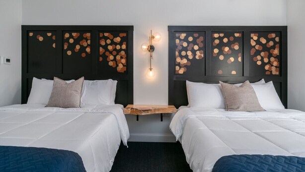 Et hotelværelse med to senge, et trænatbord og en vægmonteret lampe.