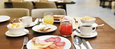 A breakfast table set with plates of food, including eggs, tomatoes, and ham, along with cups of coffee and juice.