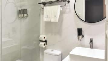A modern bathroom with a glass shower enclosure, a white sink, a toilet, and a towel rack with folded towels.