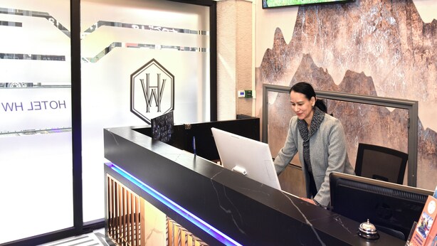 Een modern ogend receptiebalie met een digitaal scherm en een bord met de naam van het hotel.