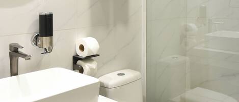 A modern bathroom with a large oval mirror, a white sink, a toilet, and a glass-enclosed shower area.