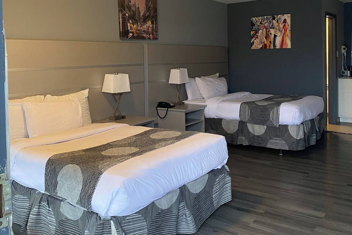 A hotel room with two beds, a nightstand, a lamp, a painting, and a ceiling light.