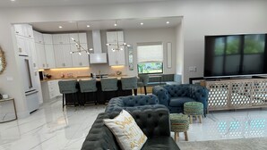 Een moderne woonkamer met een hoekbank, een televisie en een keuken met witte kasten en barstoelen.