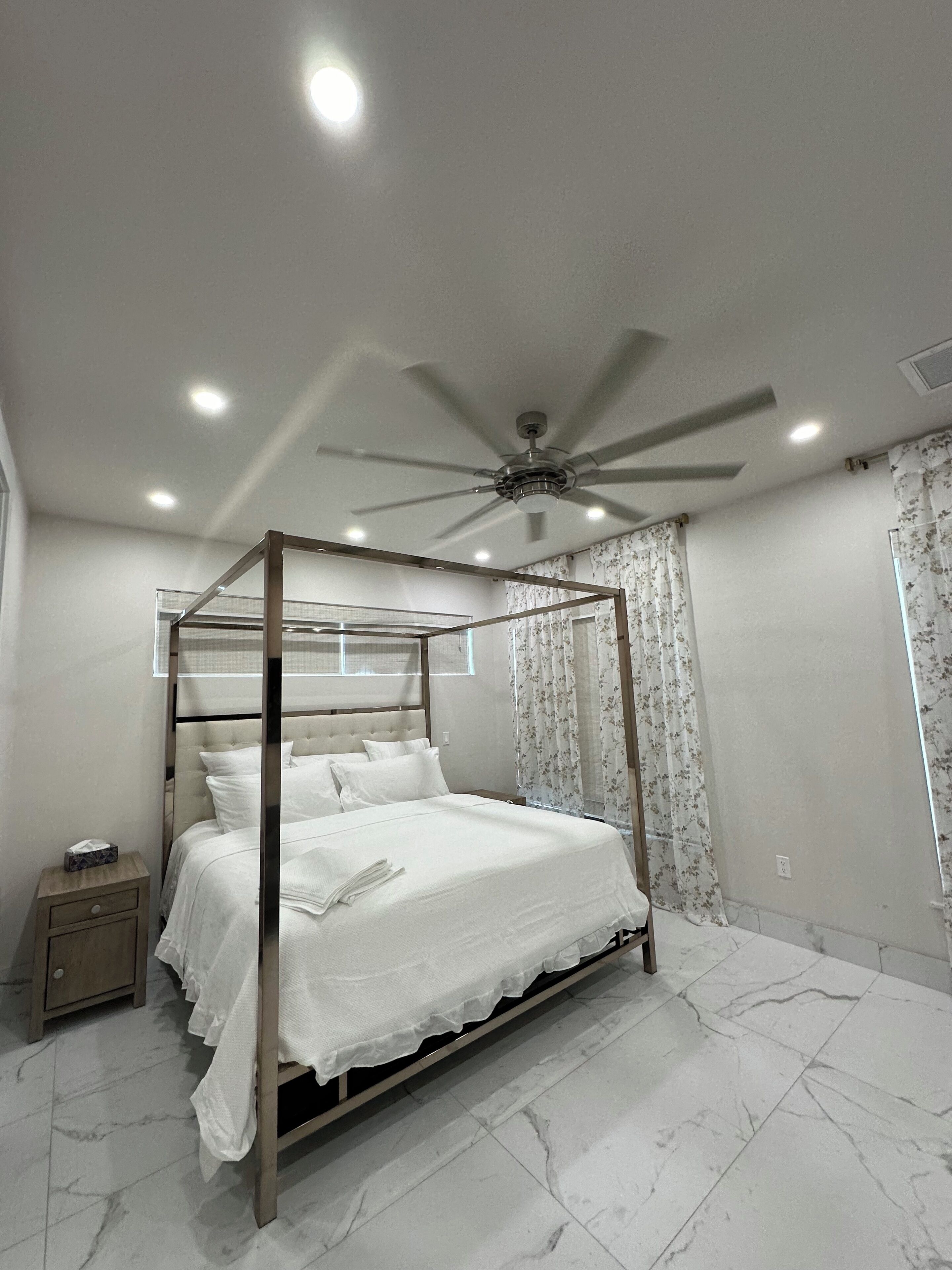 A four-poster bed with a ceiling fan, a bedside table, and a nightstand.