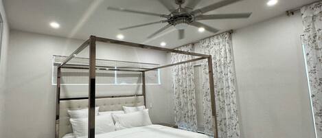 A four-poster bed with a ceiling fan, a bedside table, and a nightstand.