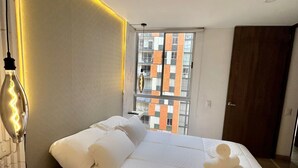 Une chambre d’hôtel avec un grand lit, une table de chevet, une lampe et une vue sur un immeuble aux panneaux orange et blancs.