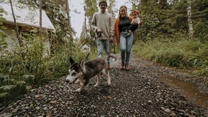 Una familia paseando un perro por un sendero de grava rodeado de follaje.