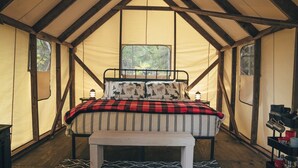 Una habitación con tienda de campaña acogedora, con cama, un banco y una pequeña mesa con un farol.