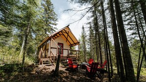 Una cabaña en un bosque con una terraza y mobiliario exterior.