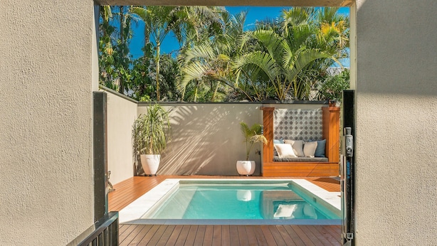 A swimming pool with a wooden deck, a seating area with cushions, and a wall with a patterned design.