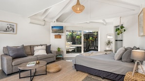 A modern living room with a sofa, a coffee table, a bed, and a large window overlooking a garden.