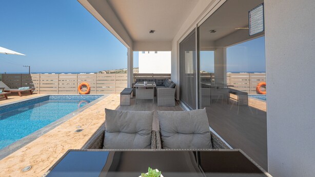 A poolside area with a seating arrangement, a small table with a plant, and a view of the beach and ocean.