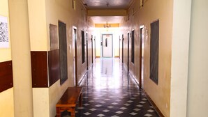 A long hallway with a checkered floor, doors on both sides, and a wooden bench in the center. - Sri sapthagiri lodge (Chirala)
