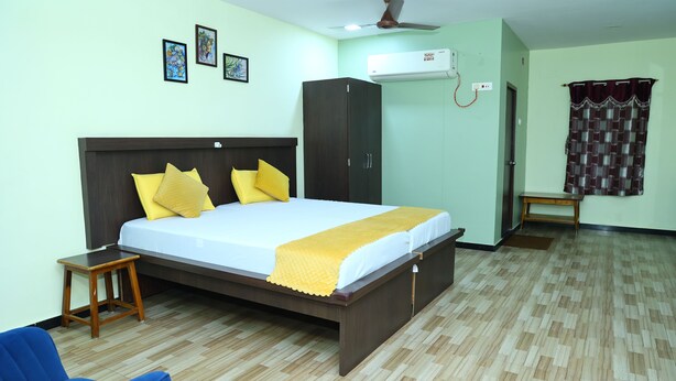 A bedroom with a bed, a wardrobe, a chair, and an air conditioning unit. - Sri sapthagiri lodge (Chirala)
