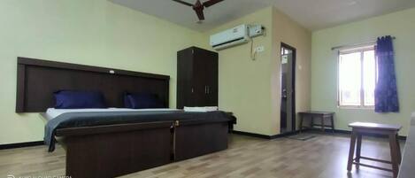 A bedroom with a bed, wardrobe, air conditioning unit, and a window with curtains.