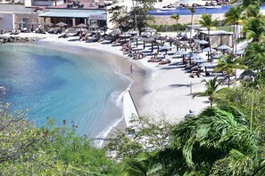 A beach resort with sun loungers, umbrellas, and a clear blue pool.