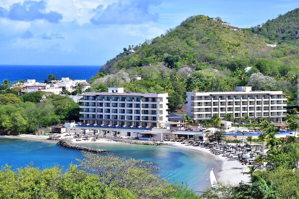 A coastal hotel with multiple buildings, a beach, and a mountainous backdrop.