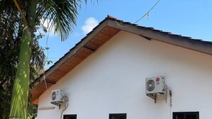 A white building with two air conditioning units mounted on the exterior wall, a small window, and a roof with a wooden section. - Home Investments Villa (Moshi)