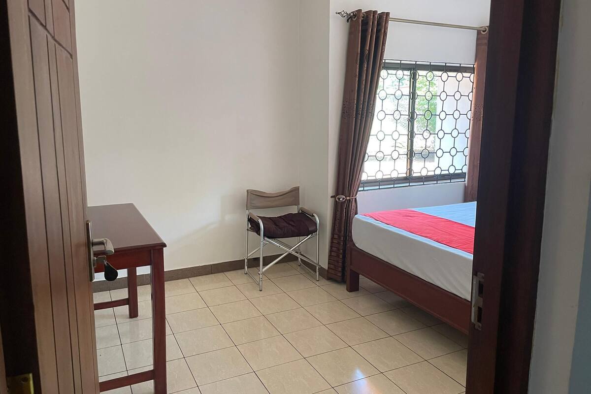 Une chambre à coucher avec un lit, une chaise, une table et une fenêtre avec des rideaux.