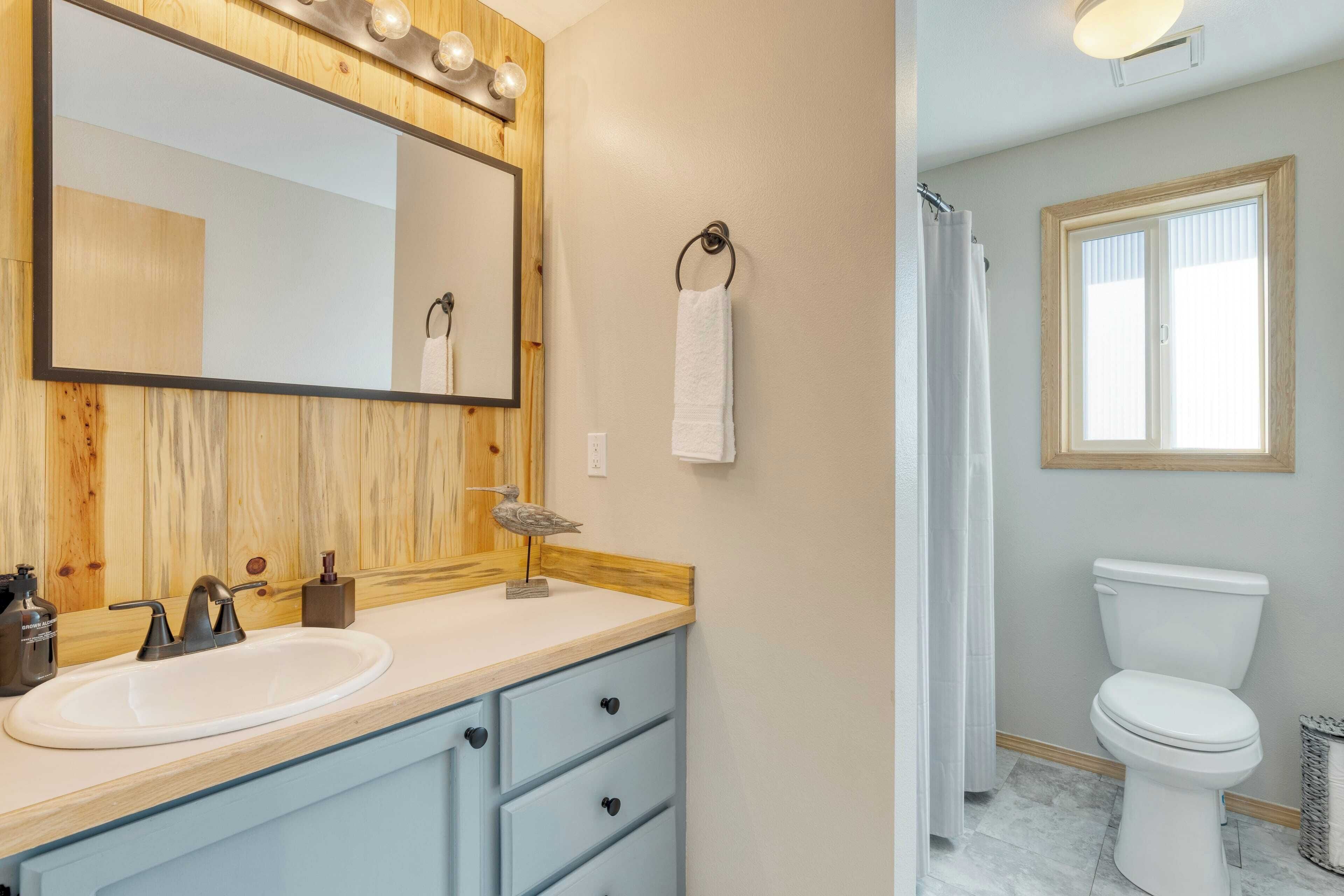 A bathroom with a wooden vanity, a large mirror, a white sink, a towel ring, a toilet, and a window.