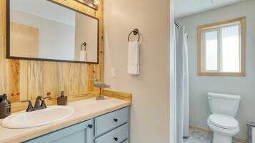 A bathroom with a wooden vanity, a large mirror, a white sink, a towel ring, a toilet, and a window.