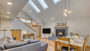 A spacious living area with a grey sofa, wooden dining table, and a fireplace. - Royal Canoe by Avantstay Walk to the Shore + Cozy Fireplace (Arch Cape)