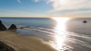 Uma praia com céu claro, mar calmo e afloramentos rochosos.