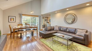 A spacious living room with a wooden dining table, a leather sofa, and a large mirror on the wall. - Royal Canoe by Avantstay Walk to the Shore + Cozy Fireplace (Arch Cape)