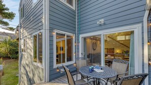 A patio with a round table and chairs, a covered area with a glass door, and string lights. - Royal Canoe by Avantstay Walk to the Shore + Cozy Fireplace (Arch Cape)