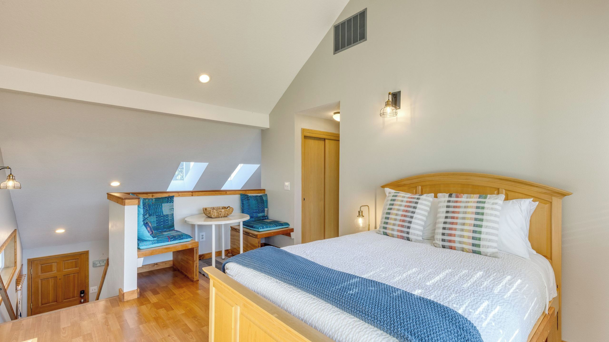 A bedroom with a bed, a bench with cushions, a small table, and a window.