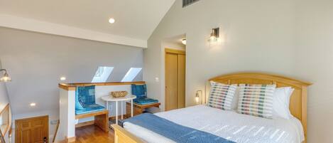 A bedroom with a bed, a bench with cushions, a small table, and a window.
