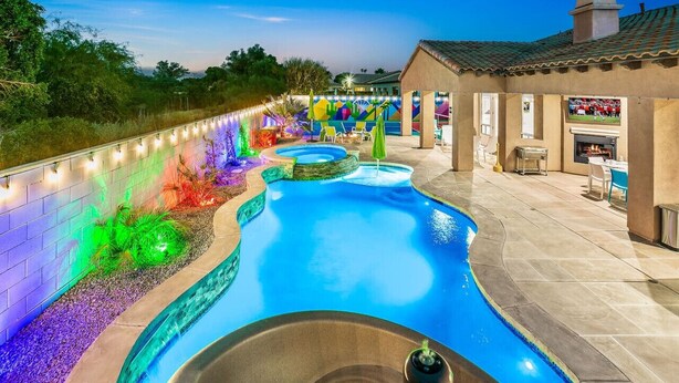 Une piscine au design incurvé, entourée d’un espace paysager agrémenté d’un éclairage coloré. On y trouve également un bâtiment doté d’une terrasse et d’un espace barbecue extérieur.