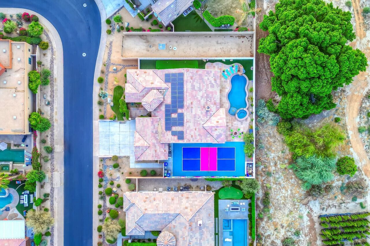 Vista aérea de una propiedad residencial con piscina, cancha de tenis y jardín ajardinado.