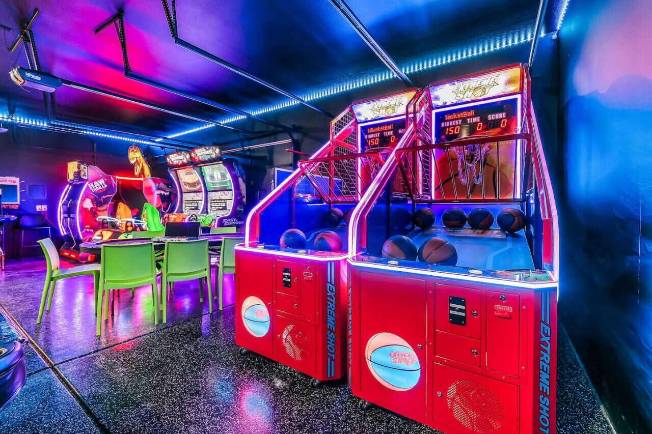 Eine hell erleuchtete Spielhalle mit Neonlichtern und verschiedenen Spielautomaten, darunter Basketball- und Greifautomaten.