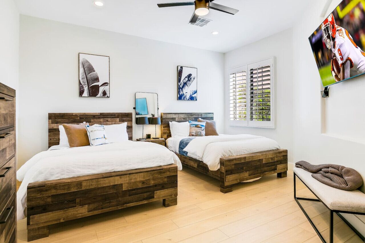 A bedroom with two wooden beds, a ceiling fan, and a TV on the wall.