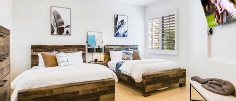 A bedroom with two wooden beds, a ceiling fan, and a TV on the wall.
