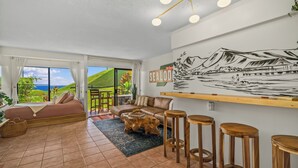 Un salón amplio con una cama grande, un sofá y una mesita de centro. Hay un mural en la pared y vistas al exterior.