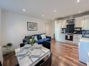 A modern kitchen with white cabinets, a dining area with a table set for four, and a blue sofa in the living area.